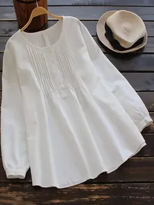 Close-up of white linen-cotton blouse showing pleated details and buttoned round neck