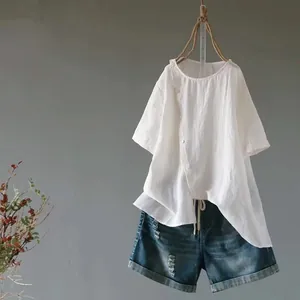 Weiße Baumwoll-Leinen-Bluse mit unregelmäßigem Saum und Jeans-Shorts an der Wand
