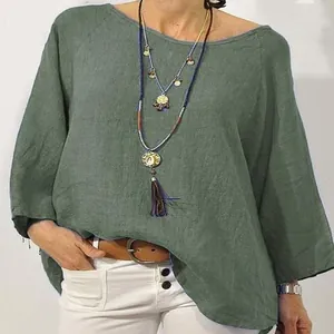 Dettaglio ravvicinato di una camicetta in lino verde con maniche raglan e scollo rotondo.