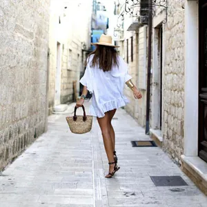 Γυναίκα με λευκό ριχτό κάλυμμα παραλίας με βολάν και ψάθινο καπέλο σε πέτρινο σοκάκι