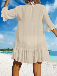 Rückansicht einer Frau in einem beigen Strandkleid mit Rüschen an einem sonnigen Strand