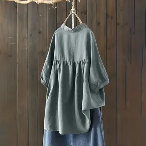 Back view of a grey blue cotton linen long sleeve shirt with pleated waist hanging on wood.