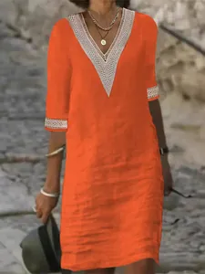 Detail view of orange V-neck dress with intricate lace trim and medium sleeves