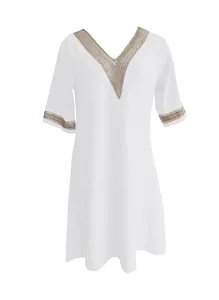Detailed close-up of a white cotton linen V-neck dress with decorative golden lace trim
