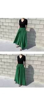 Close-up of green linen wide-leg pants paired with a black ribbed top against a stone wall.