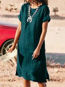 Woman wearing dark teal textured short sleeve dress with side slits in desert setting