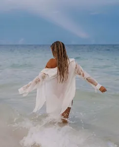 Mujer con camisa de playa blanca caminando hacia las olas del mar, vista trasera