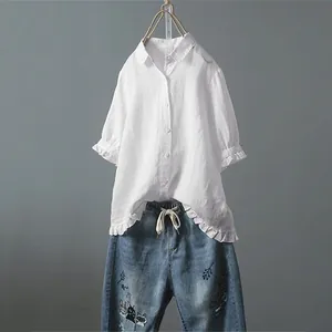 Detailansicht einer weißen Baumwoll-Leinenbluse mit Rüschen und bestickten Jeans.
