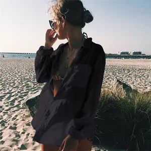 Mujer elegante con una camisa de playa negra de gran tamaño en una playa soleada.