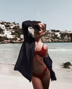 Camisa playera negra de gran tamaño sobre un bikini rojo en una playa soleada.