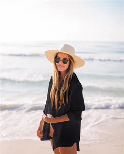 Hermosa mujer con un camisón de playa negro y un sombrero de paja en la playa soleada