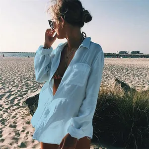 Mujer elegante con un pareo blanco tipo camisa de gran tamaño en una playa soleada