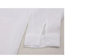 Primer plano del puño con botón de una túnica playera blanca de tela ligera y suave