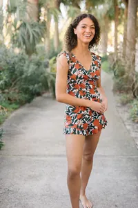 Model wearing a summer floral orange print V-neck romper with ruffle details outdoors