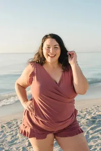 Close-up of a plus-size mauve sleeveless romper with ruffle hem details on a sunny beach.