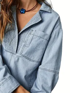 Dettaglio della giacca in denim azzurro con scollo a V plissettato e tasca borchiata