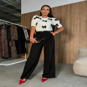 Elegante pantalón negro de talle alto y pernera ancha con un jersey de lazos blancos