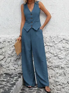 Model posing in blue linen vest and trousers set against a white textured wall backdrop