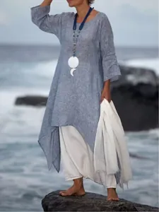 Model wearing a loose-fitting blue linen maxi dress with asymmetrical hem on rocky seaside