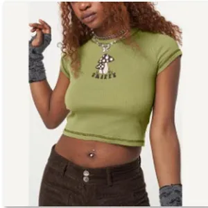 Λεπτομερής προβολή ενός ανοιχτόπράσινου crop top με γραφικό μανιτάρι και κείμενο fairy's