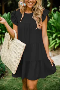 Detail of a black summer dress with ruffle sleeves and tiered design in outdoor setting