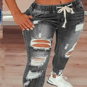 Détail d'un jean gris déchiré pour femme avec taille à cordon et une finition usée.