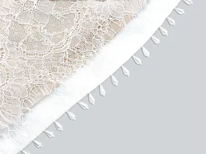 Macro detail of intricate white eyelash lace with elegant pearl bead embellishments