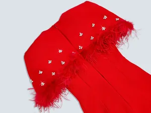 Primer plano de vestido de noche rojo con plumas de avestruz y detalles de pedrería fina