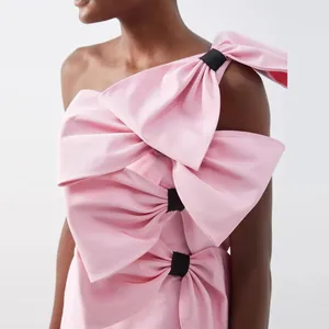 Detail view of a pink satin dress featuring large decorative bows on the bodice