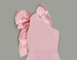 Close-up detail of a pink one-shoulder dress featuring a large satin bow and ribbed texture.