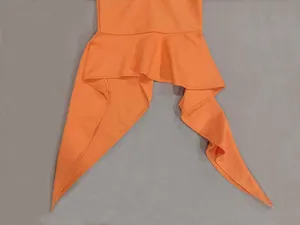 Primo piano dell'orlo arancione con volant su abito in maglia asimmetrico.