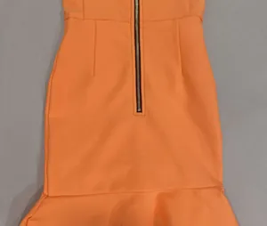 Dettaglio dell'abito lungo in maglia arancione con cerniera nera e orlo a volant.