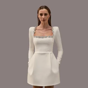 Detailed view of white long-sleeve dress featuring a rhinestone-embellished square neckline