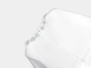 Macro close-up of elegant crystal flower embellishments and invisible zipper on a white jumpsuit.