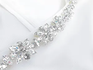 Close-up detail showing the sparkling rhinestone flower embellishment on a white jumpsuit