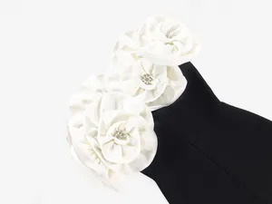 Close-up of elegant white fabric flowers with crystals on a black bandage dress.