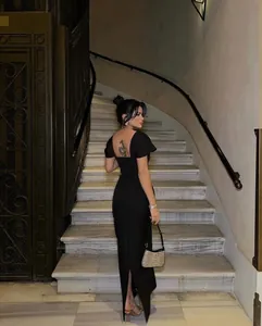 Elegant black backless bandage evening dress shown on staircase with rhinestone bag
