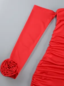 Close-up of 3D rose flower detail on sleeve and ruched fabric of red dress.