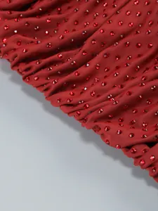 Close-up of red rhinestones on a burgundy evening dress fabric showing fine details.
