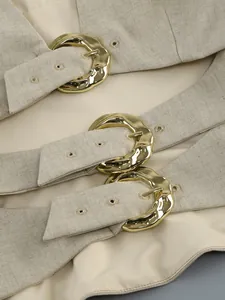 Detailed close-up showing three polished gold buckles on beige linen-textured garment straps