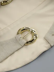 Detail of a textured beige garment featuring a unique golden hammered metal buckle