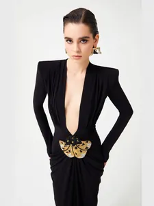 Elegant black long-sleeved deep V-neck dress with gold butterfly ornament at waist.