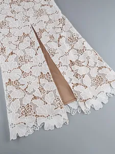 Close-up detail of white floral lace fabric with tan lining and delicate scalloped hem