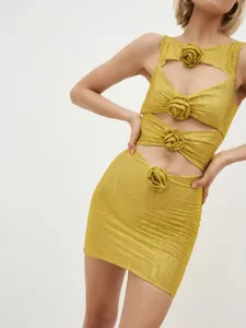 Detail eines goldenen Mini-Kleides mit Strass, Cut-outs und 3D-Blumenverzierung.