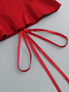 Dettaglio dell'orlo di un abito a corsetto rosso con pieghe e lunghi nastri di raso