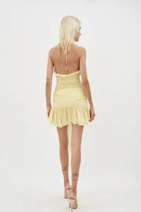 Back view of a yellow halter neck ruched mini dress with ruffle hem details.