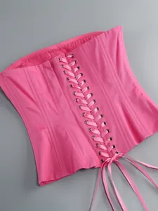 Dettaglio di un corsetto stringato rosa vibrante con nastro di raso su sfondo grigio