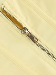 Dettaglio macro di una cerniera in metallo dorato di qualità su un capo giallo pallido.