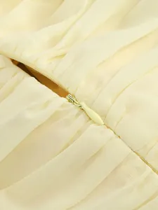 Close-up detail of a hidden zipper on a luxury pleated yellow chiffon dress fabric.