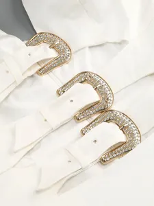 Macro detail of three elegant gold buckles with rhinestones on a white dress garment